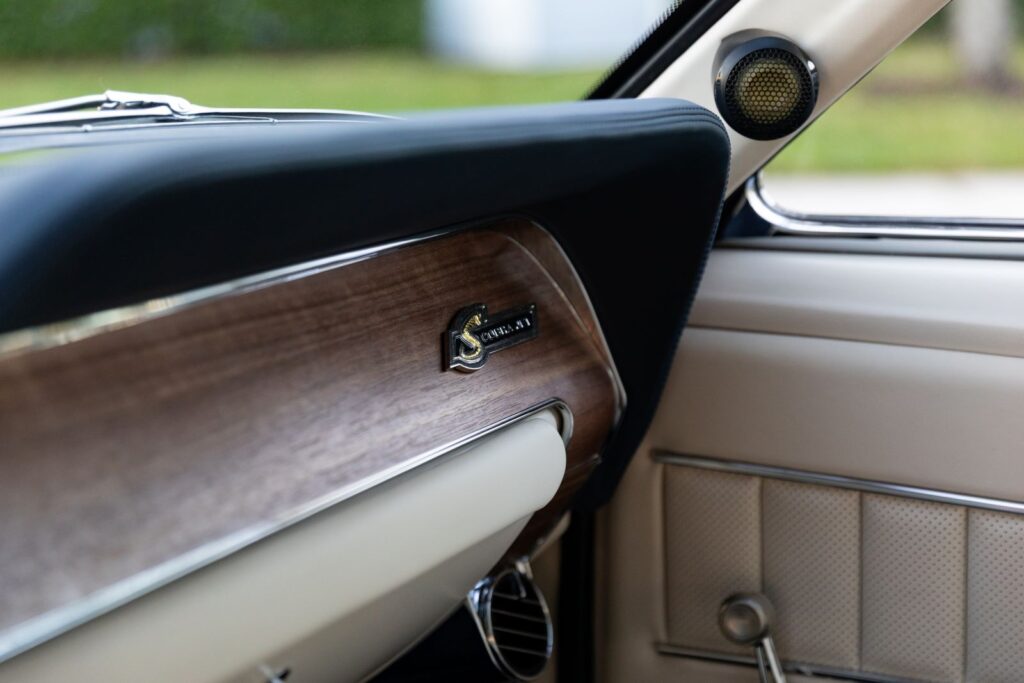 Close-up of the passenger-side wood grain dashboard with a "Shelby G.T.500KR" emblem and a modern tweeter integrated into the A-pillar of a Revology Mustang.