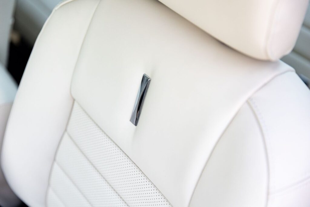 Macro view of the white leather seat back in a 1968 Revology Shelby GT500KR, featuring a chrome trim emblem and perforated leather inserts.