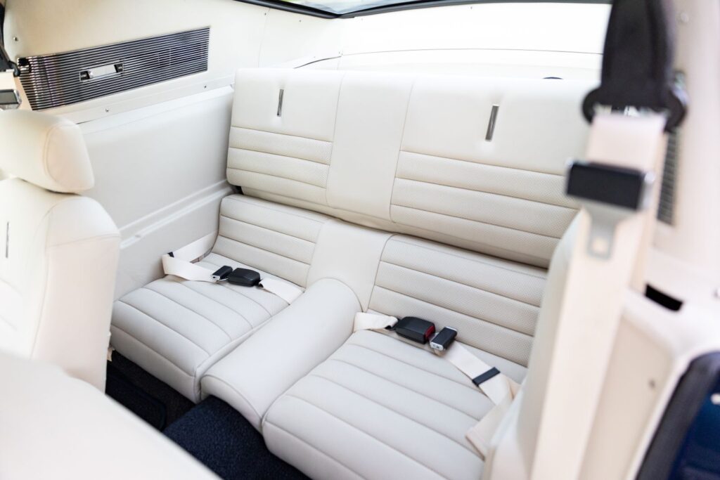 View of the white leather rear fold-down seats in a 1968 Revology Shelby GT500KR Fastback, including matching seatbelts and side trim panels.