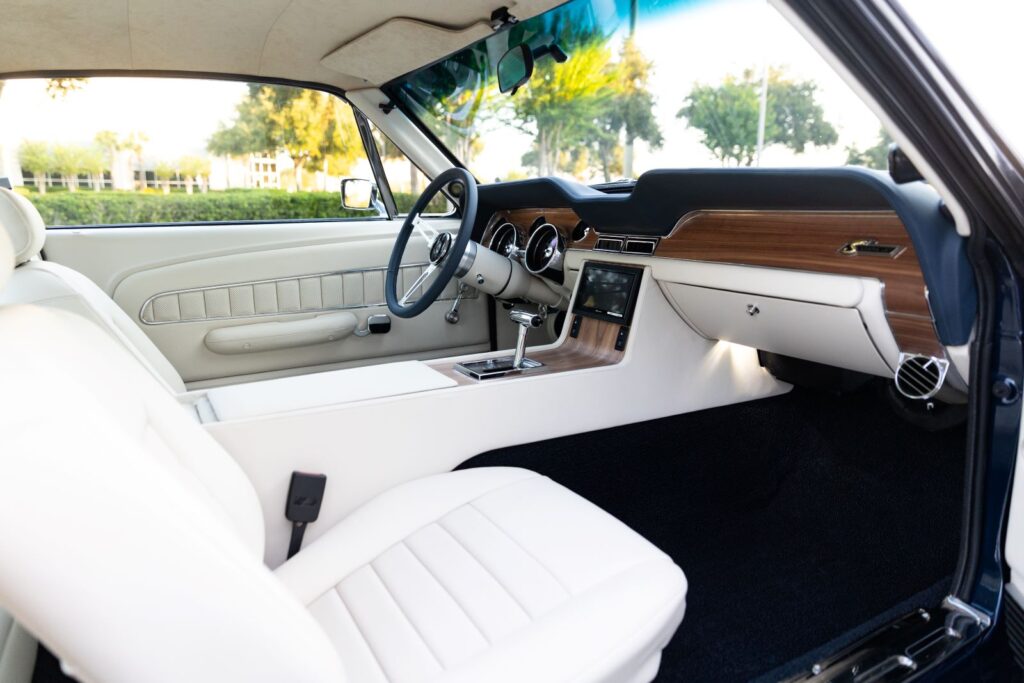 Wide-angle passenger-side view of the white leather interior in a 1968 Revology Shelby GT500KR, showcasing the full dashboard, center console, and high-back bucket seats.