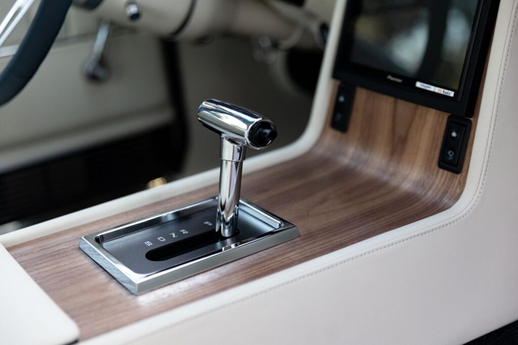 Close-up of a Pioneer touchscreen infotainment system and chrome automatic T-handle shifter in a wood grain console for a 1968 Revology Shelby GT500KR.