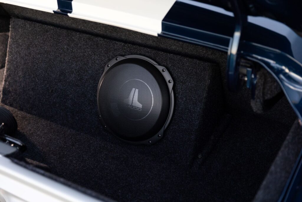 Close-up of a JL Audio subwoofer mounted in a custom-built, carpeted enclosure within the trunk of a 1968 Revology Shelby GT500KR.