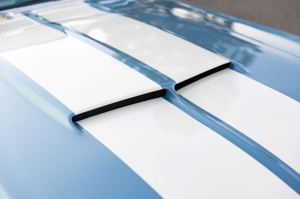Extreme close-up of the dual hood scoops on a 1967 Revology Shelby GT500 with perfectly aligned white Lemans racing stripes on a metallic blue finish.