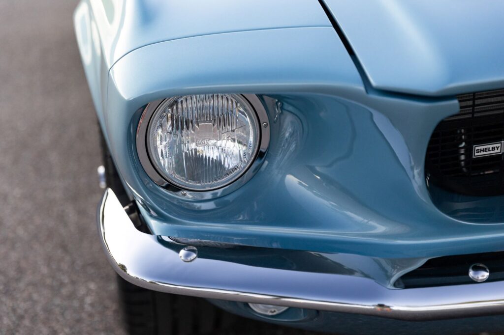 Close-up of the driver-side headlight and chrome front bumper on a metallic blue 1967 Revology Shelby GT500 Fastback.