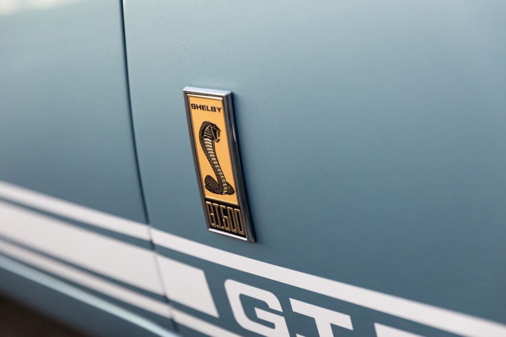 Close-up of the Shelby GT500 Cobra emblem and white side rocker stripes on a metallic blue fender of a 1967 Revology Fastback.