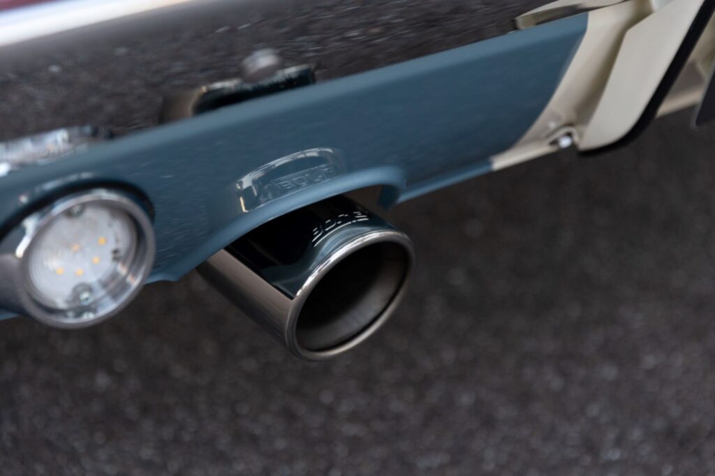Close-up of a polished stainless steel dual exhaust tip integrated into the rear valance of a metallic blue 1967 Revology Shelby GT500.