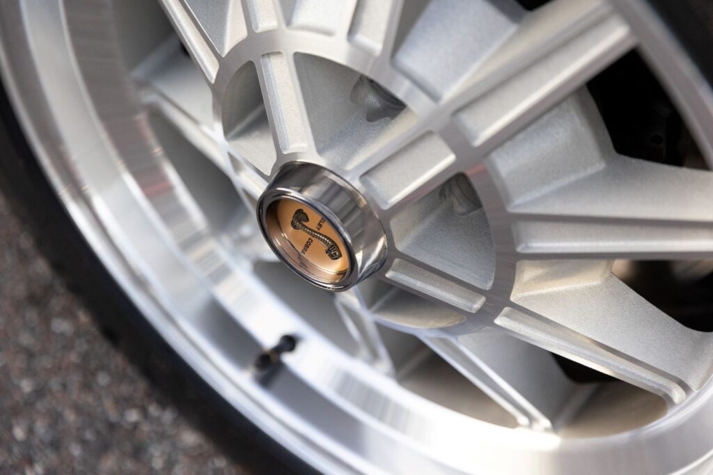 Extreme close-up of a machined aluminum wheel hub featuring a gold and black Shelby Cobra center cap on a Revology 1967 GT500.