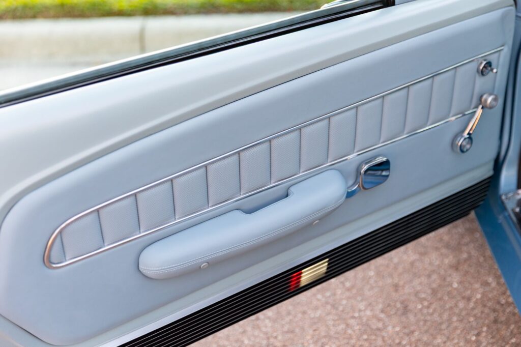 Interior view of a 1967 Revology Shelby GT500 door panel featuring light blue premium leather, chrome trim, and an integrated armrest.