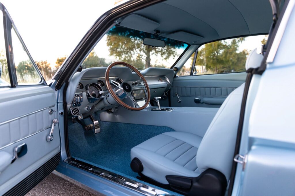 Full interior view of a 1967 Revology Shelby GT500 featuring light blue leather bucket seats, a classic wood-rimmed steering wheel, and a custom center console.