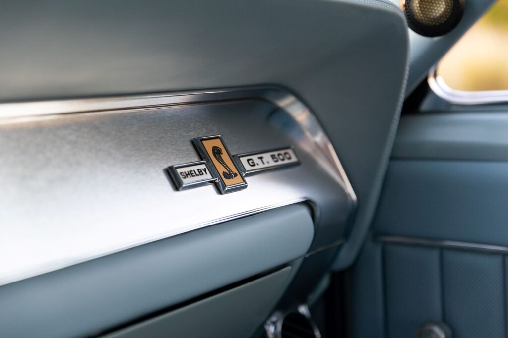 Close-up of the Shelby G.T. 500 Cobra badge mounted on a brushed aluminum dashboard panel in a 1967 Revology Mustang.