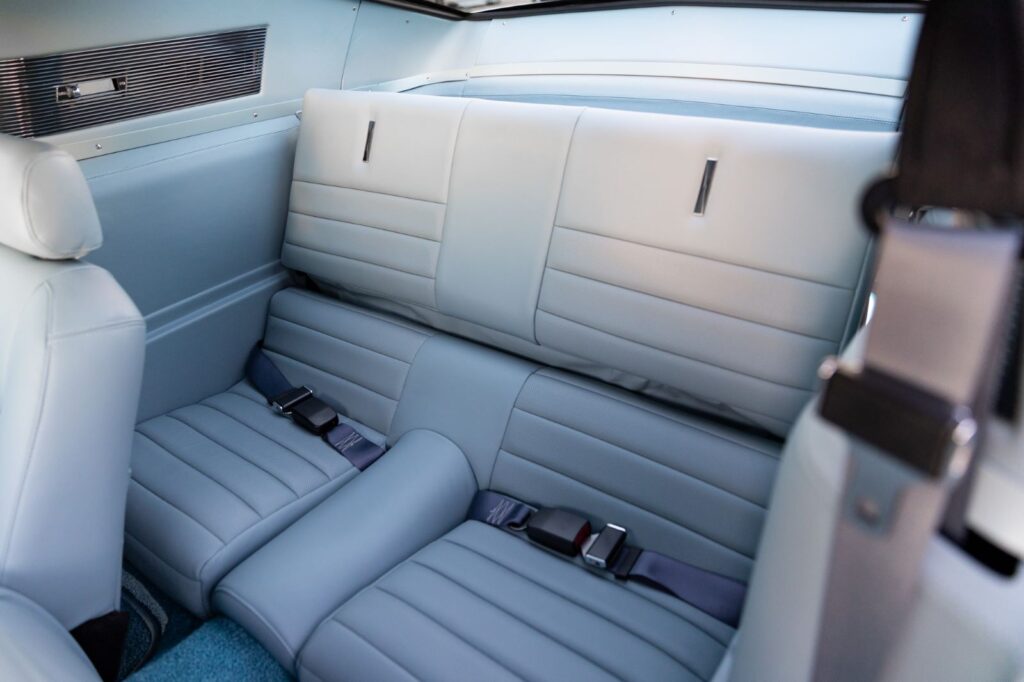 Rear interior view of a 1967 Revology Shelby GT500 Fastback showing the light blue leather rear bench seat with modern three-point seat belts.
