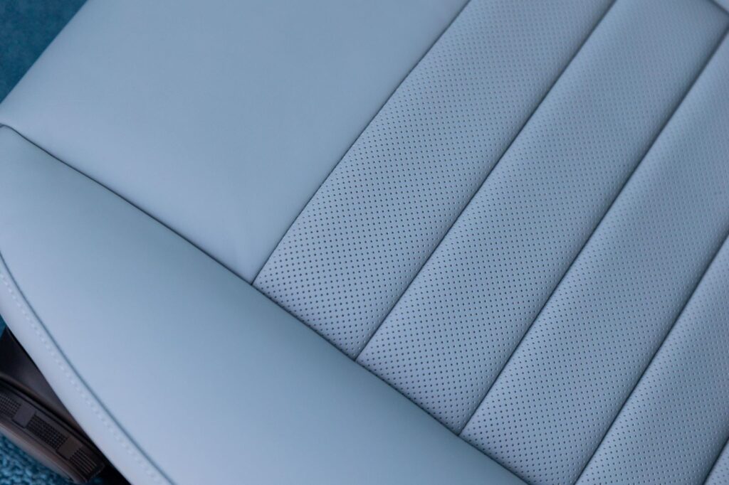 Close-up detail of light blue perforated leather upholstery with horizontal stitching on a Revology 1967 Shelby GT500 seat.