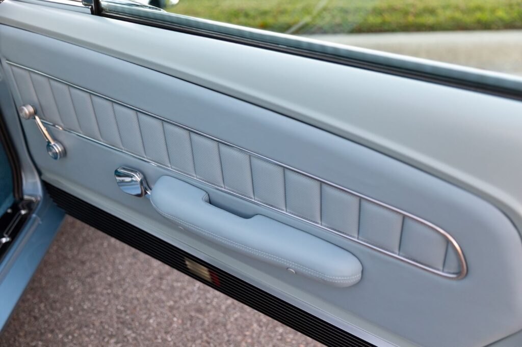 Passenger-side door panel of a 1967 Revology Shelby GT500 featuring light blue premium leather, vertical stitching, and polished chrome handles.