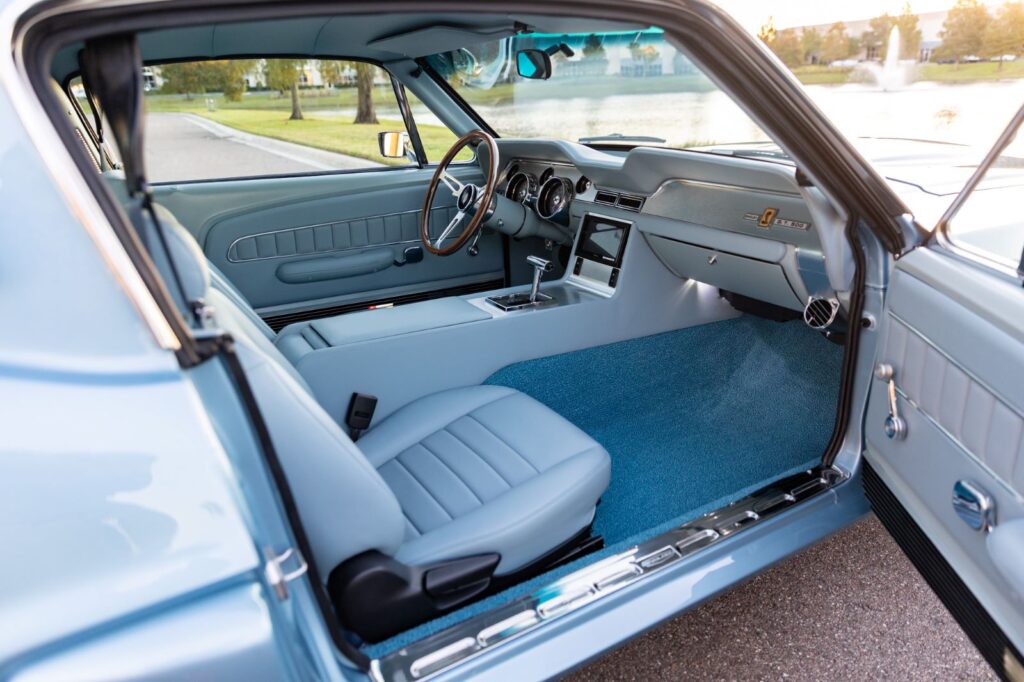 Wide-angle view of the passenger-side interior of a 1967 Revology Shelby GT500 with light blue leather bucket seats and a matching leather-wrapped dashboard.