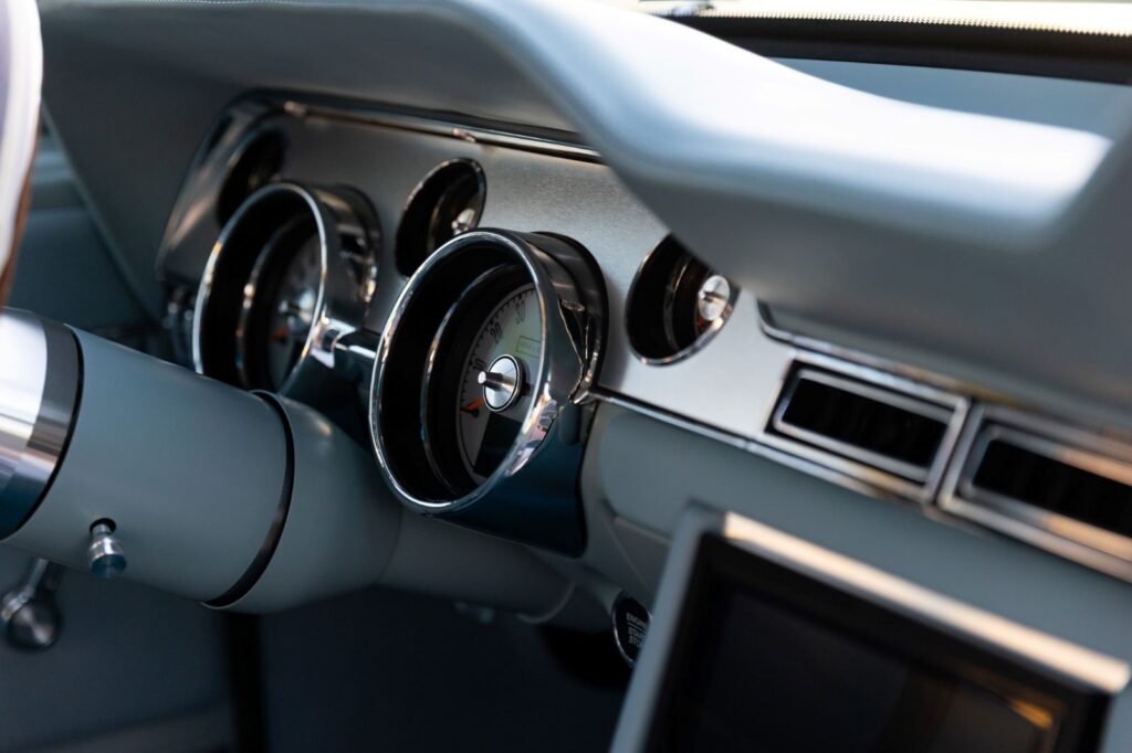 Side-angle close-up of the chrome-rimmed gauge cluster and silver dashboard trim in a 1967 Revology Shelby GT500.