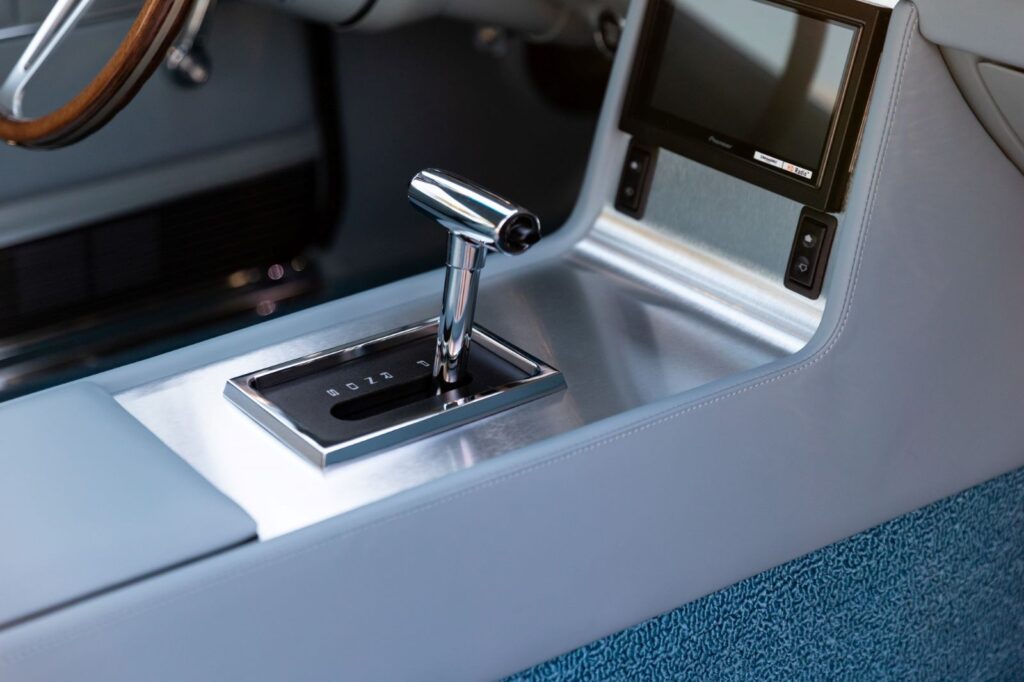 Angled view of the custom leather-wrapped center console in a 1967 Revology Shelby GT500, featuring a chrome T-handle automatic shifter and an integrated touchscreen infotainment display.