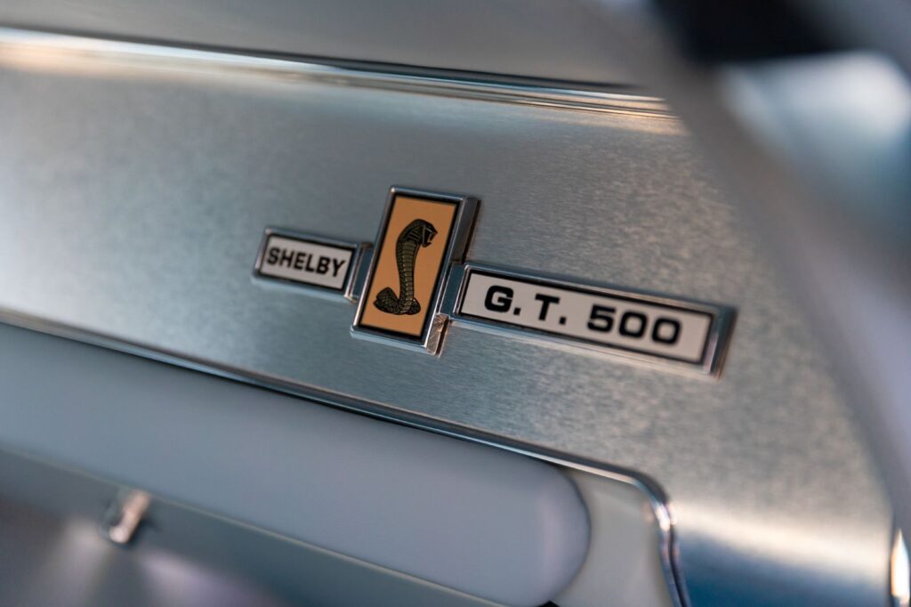 Extreme close-up of the Shelby G.T. 500 Cobra emblem mounted on a brushed metal dashboard panel in a Revology 1967 Mustang.