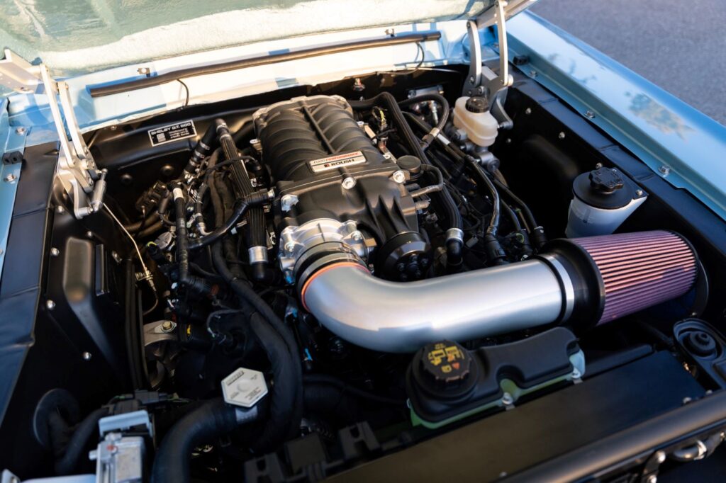 Engine bay of a 1967 Revology Shelby GT500 showing a modern supercharged Coyote 5.0L V8 engine with a custom cold air intake.