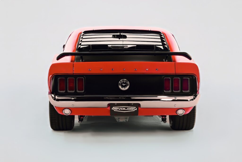 Straight-on rear view of a red Revology 1970 Ford Mustang Boss 302 restomod, featuring the signature black honeycomb tail panel, tri-bar LED taillights, rear window louvers, pedestal spoiler, and visible modern independent rear suspension.